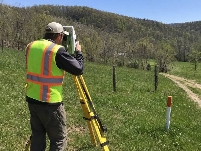 Land surveying professional locating a pipeline marker on a wooded property in Bridgeport West Virginia